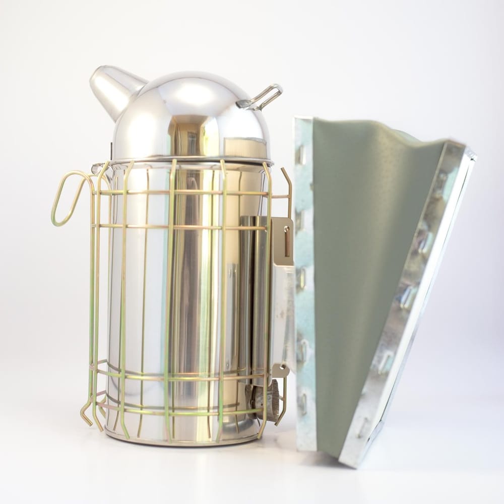 Heavy duty stainless steel beekeeping smoker resting on a wooden surface
